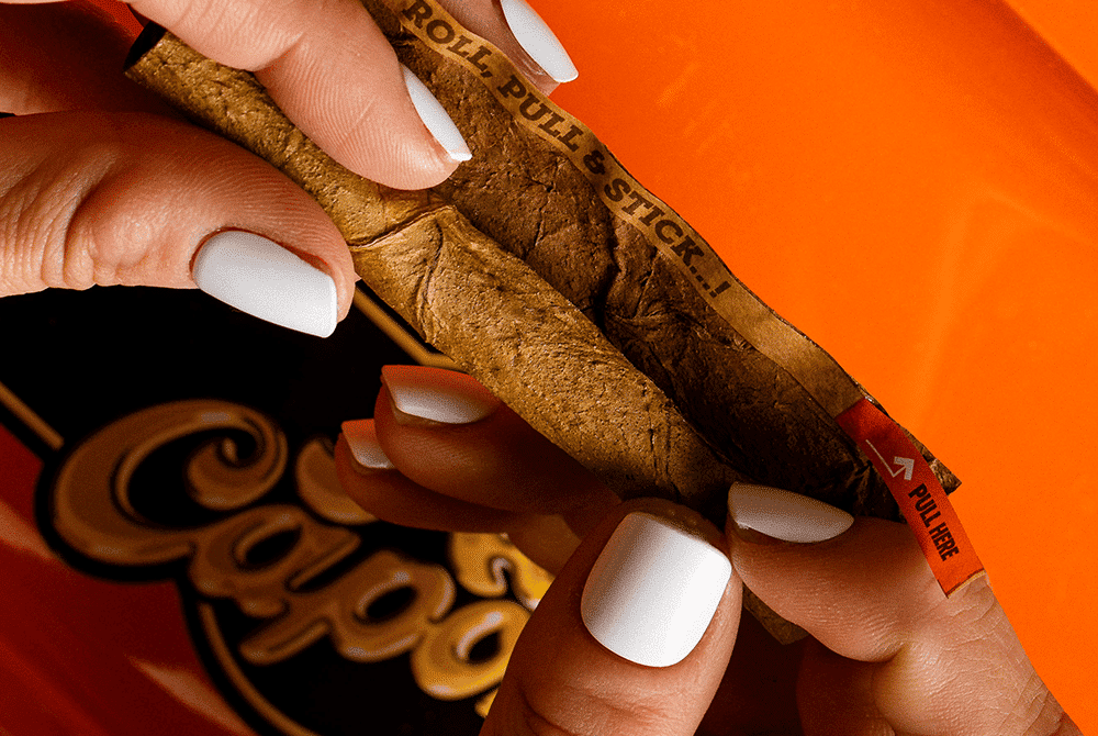 Close-up of a woman's hands rolling cannabis flower with an Al Capone leaf wrap