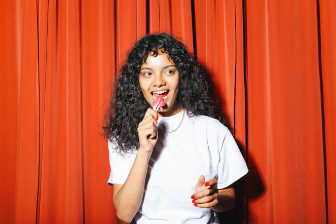 A woman is standing and bringing a gummy towards her month, while holding a package of gummies.