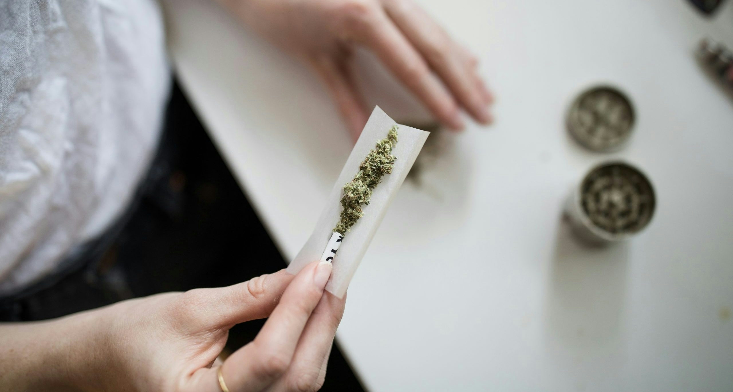 Close-up of hands rolling a cannabis joint with ground flower and rolling paper