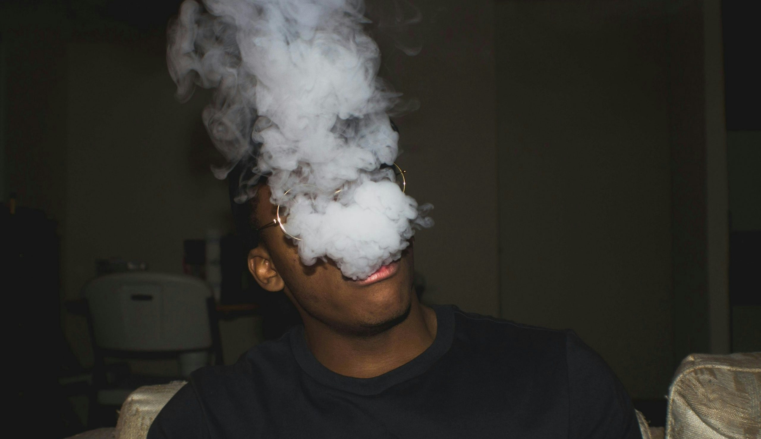 Person exhaling a thick cloud of smoke that partially covers their face