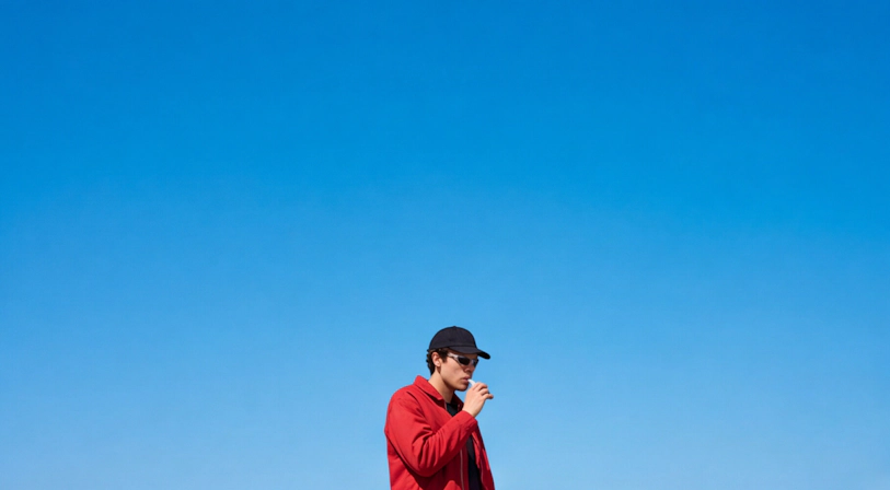 A person is standing outside with a blue sky behind them while they are standing and vaping from a liquid diamonds THCA vape.