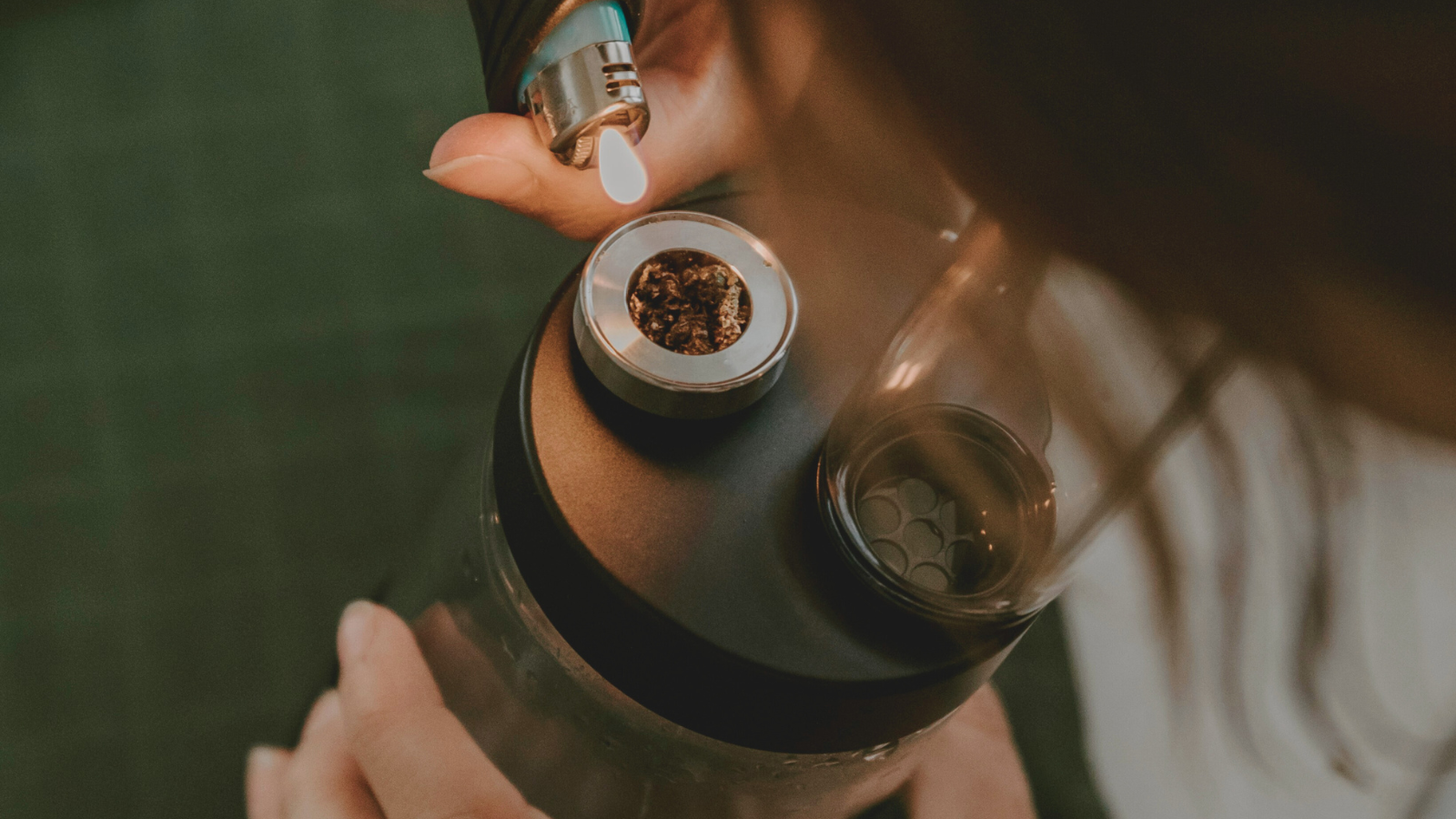 Close-up of a person lighting cannabis in a smoking device with a torch lighter
