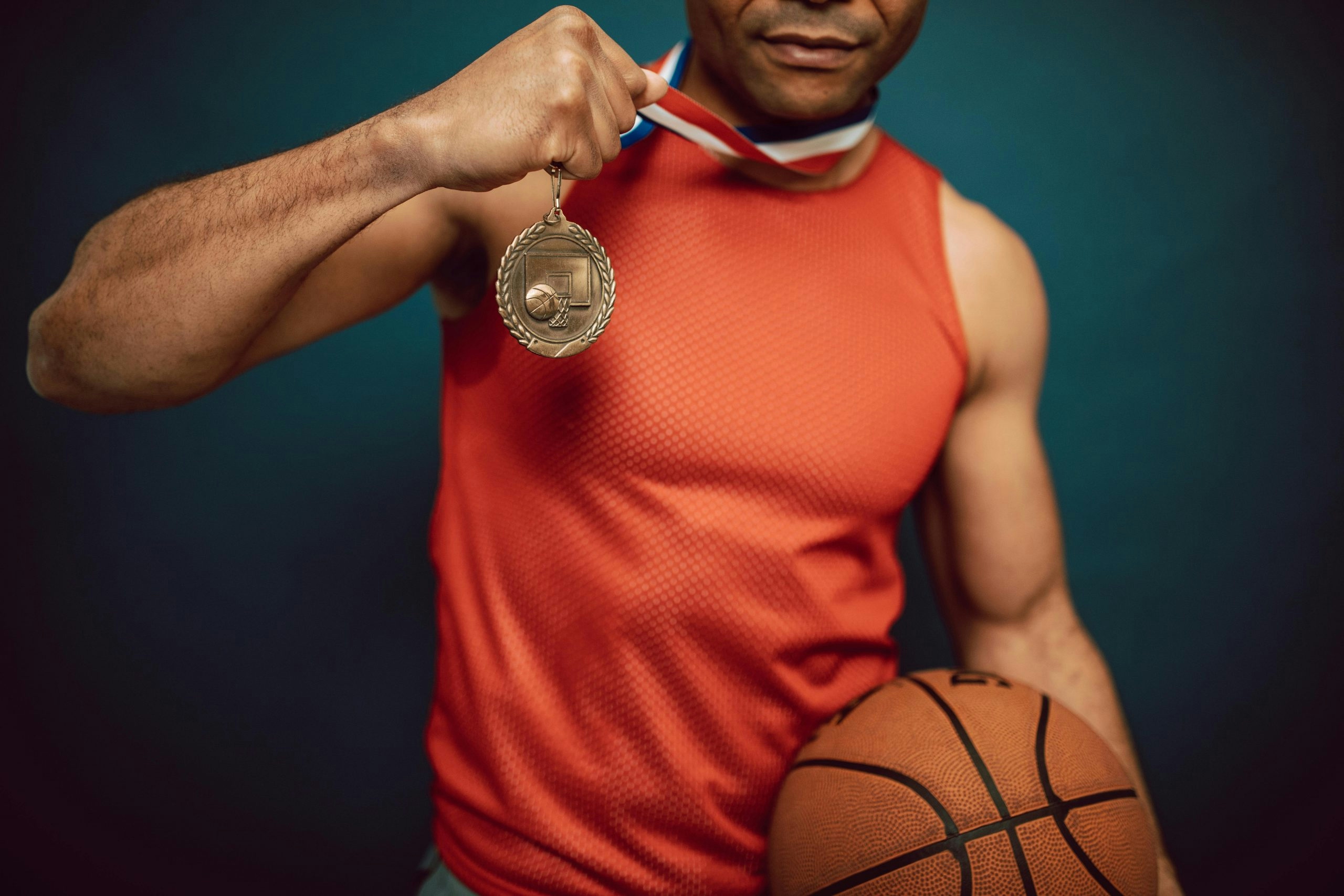 A proud man in a jersey showing a medal and holding a basketball