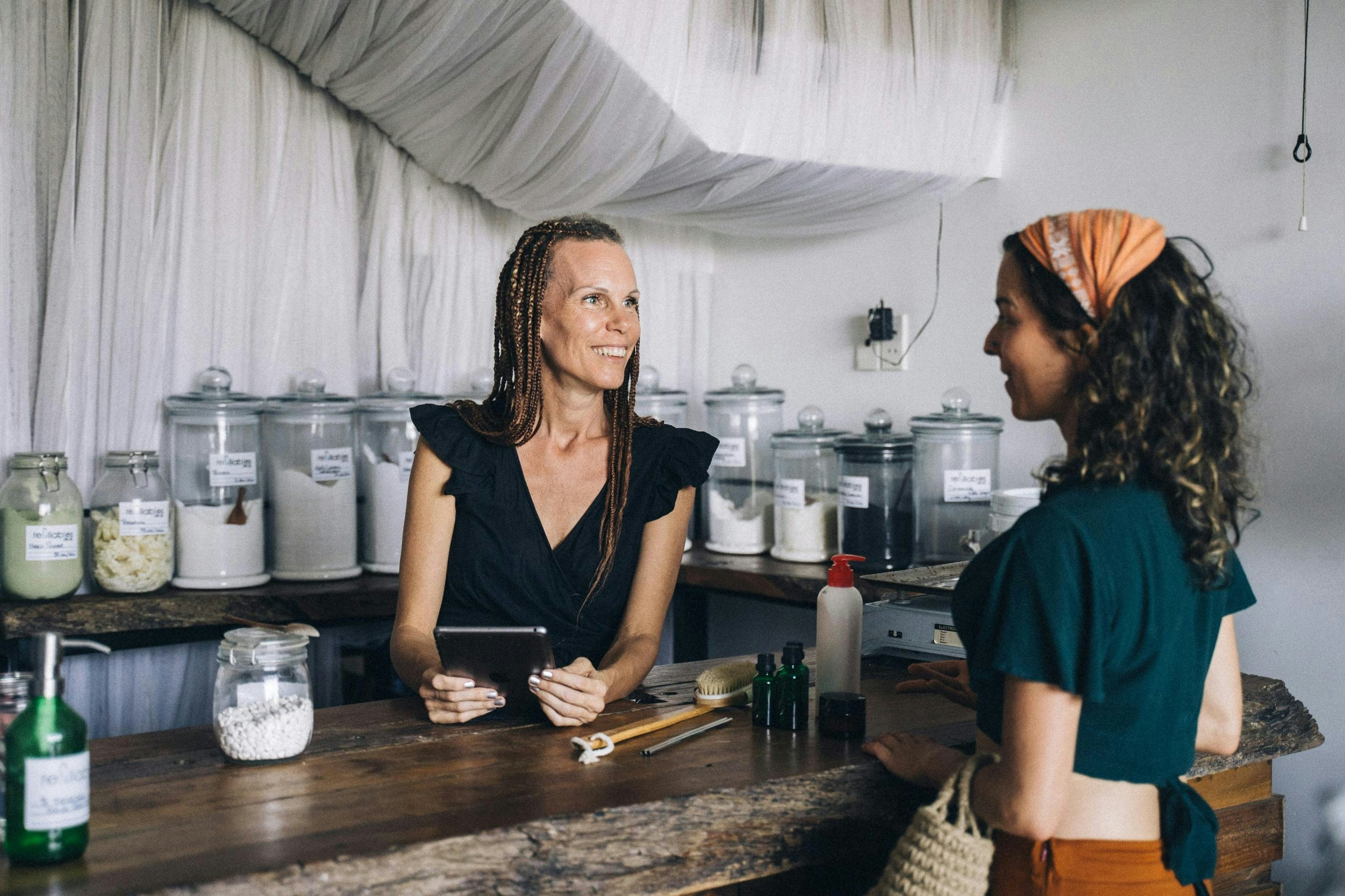 A Woman in Black Top Standing Behind a Counter Across a Woman with Orange Headscarf