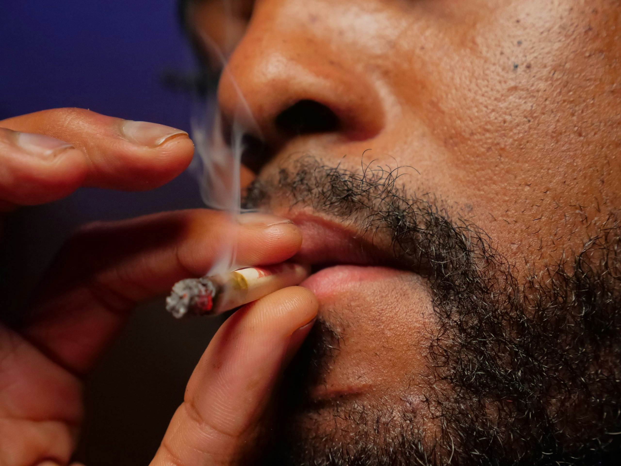 Close-up of a man's mouth inhaling a burning joint.