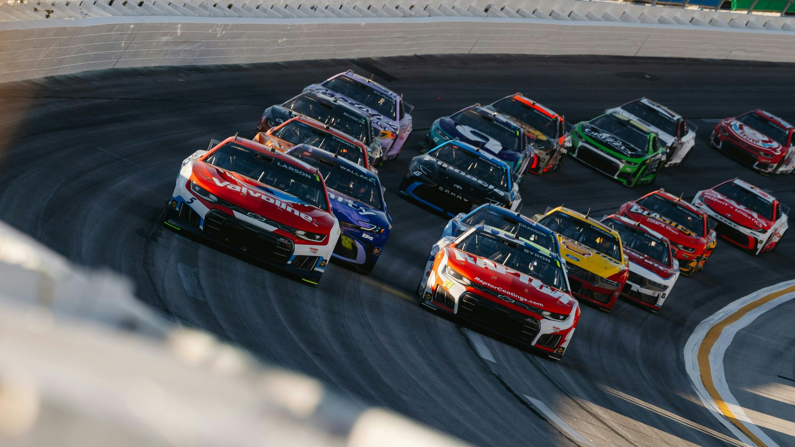 NASCAR race cars competing at high speed on a professional racetrack