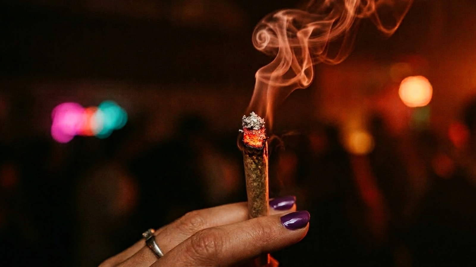 Close-up of lit joint with smoke curling, red party light, dark background