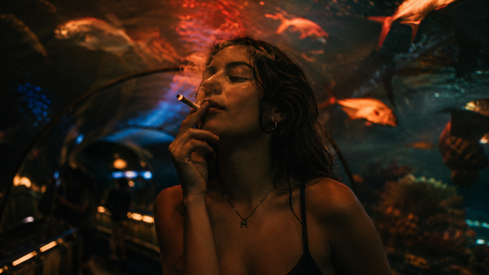 Woman smoking joint inside aquarium tunnel with fish and glowing amber lights