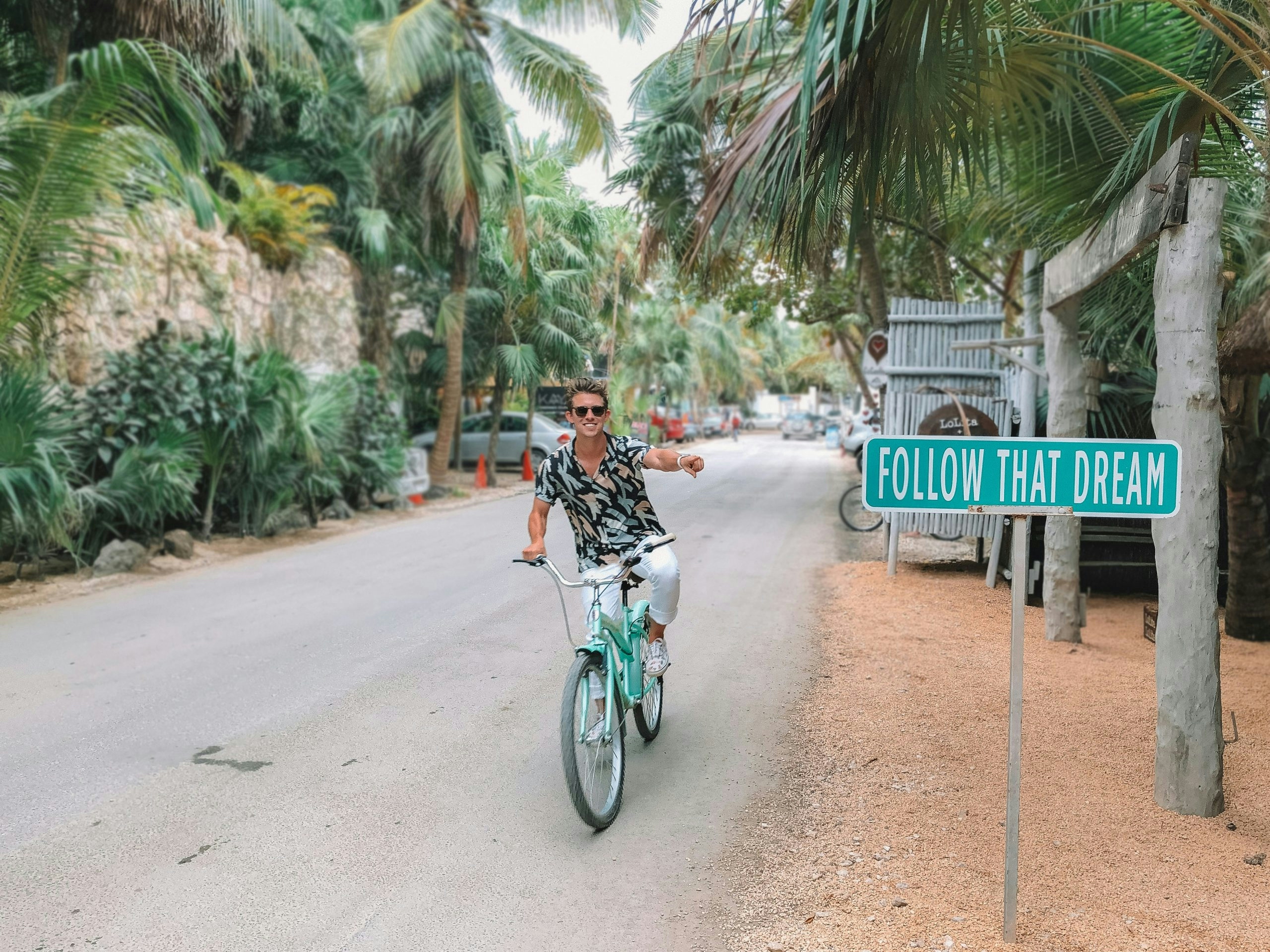 Person cycling beside a large 'Follow the Dream' sign surrounded by palm trees.