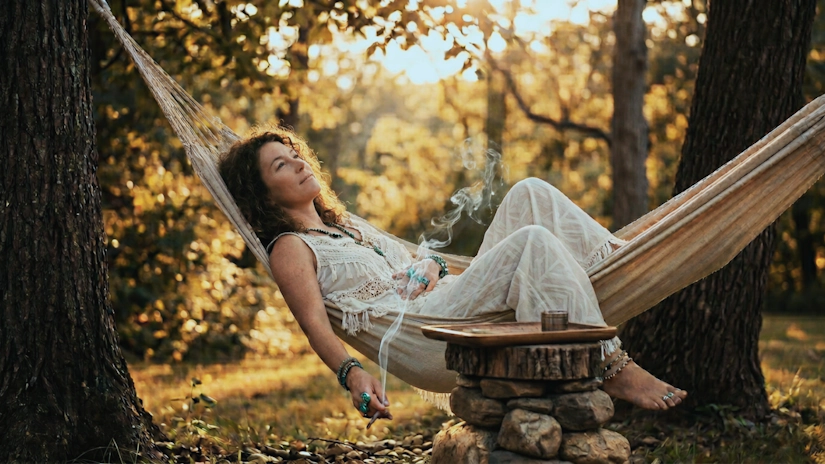 Woman relaxing in hammock with cannabis joint during golden hour forest afternoon