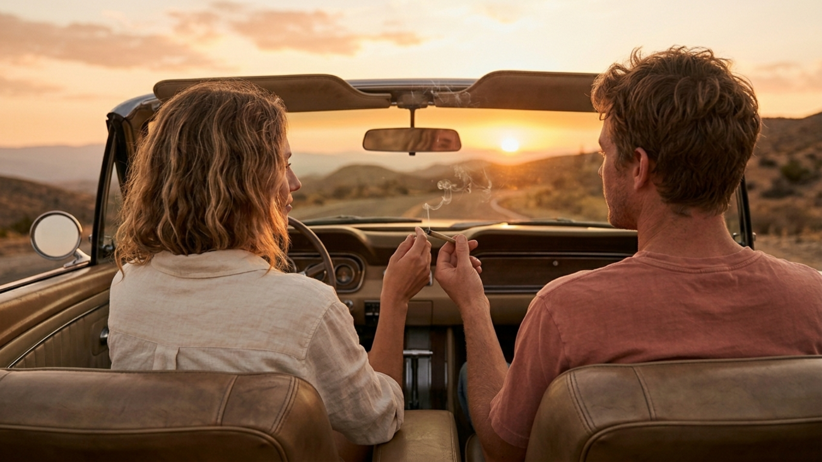 Couple in a convertible car passing a joint at sunset overlook