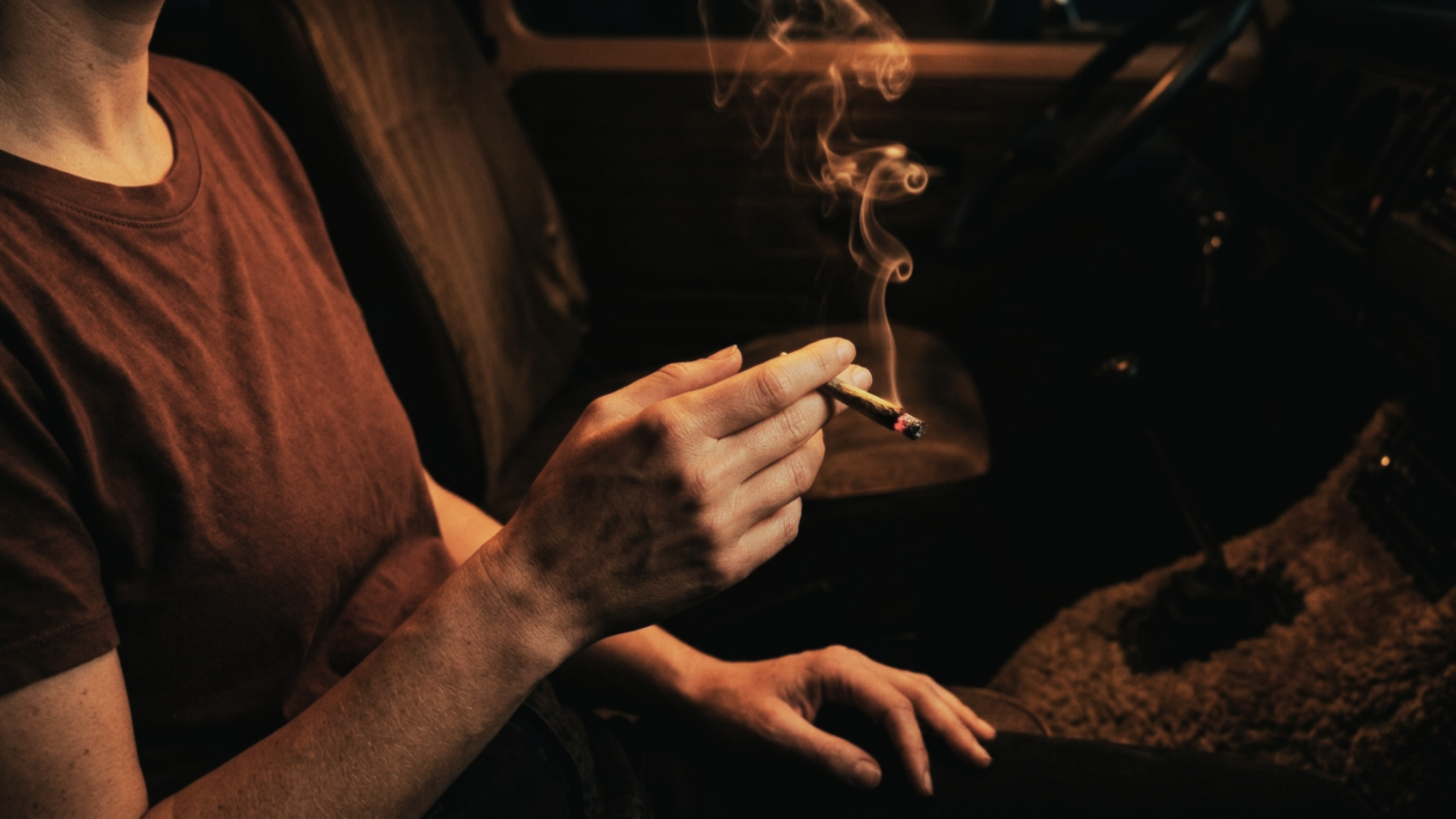 Person holding a smoking marijuana joint inside a moody vintage vehicle