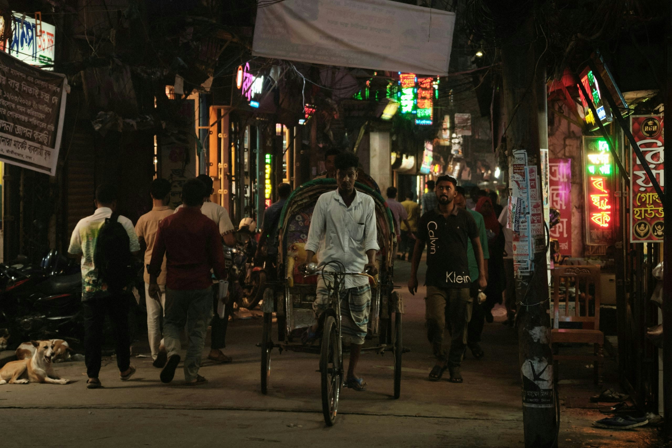 Crowded street in Dhaka filled with pedestrians, rickshaws, and local businesses