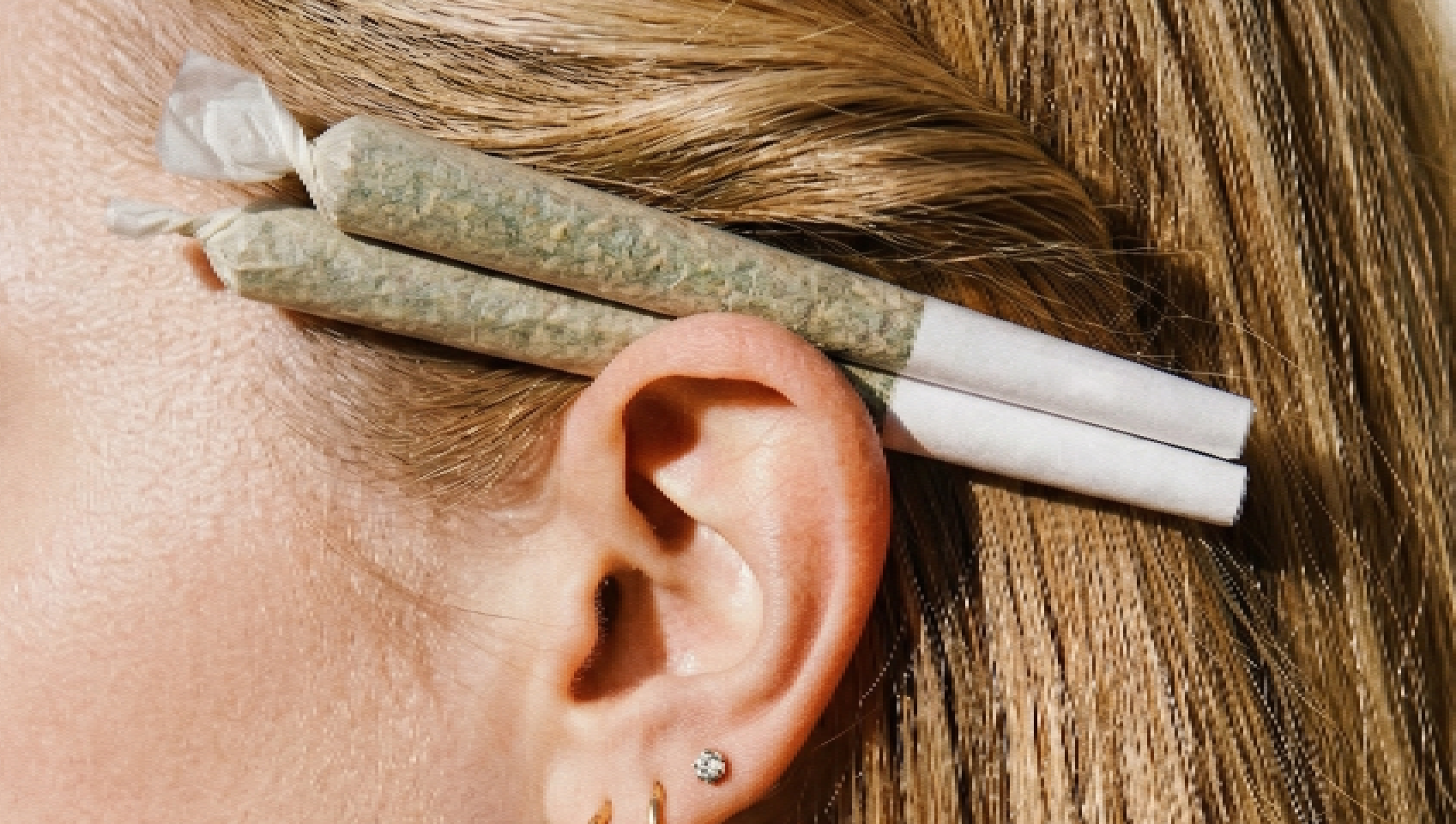 Close-up of a woman wearing two cannabis joints behind her ear with a casual lifestyle aesthetic