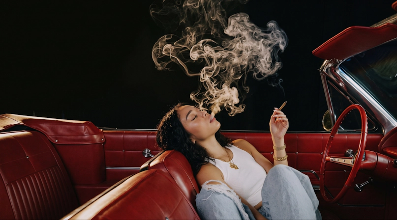 Woman smoking a cannabis joint while sitting in a parked convertible