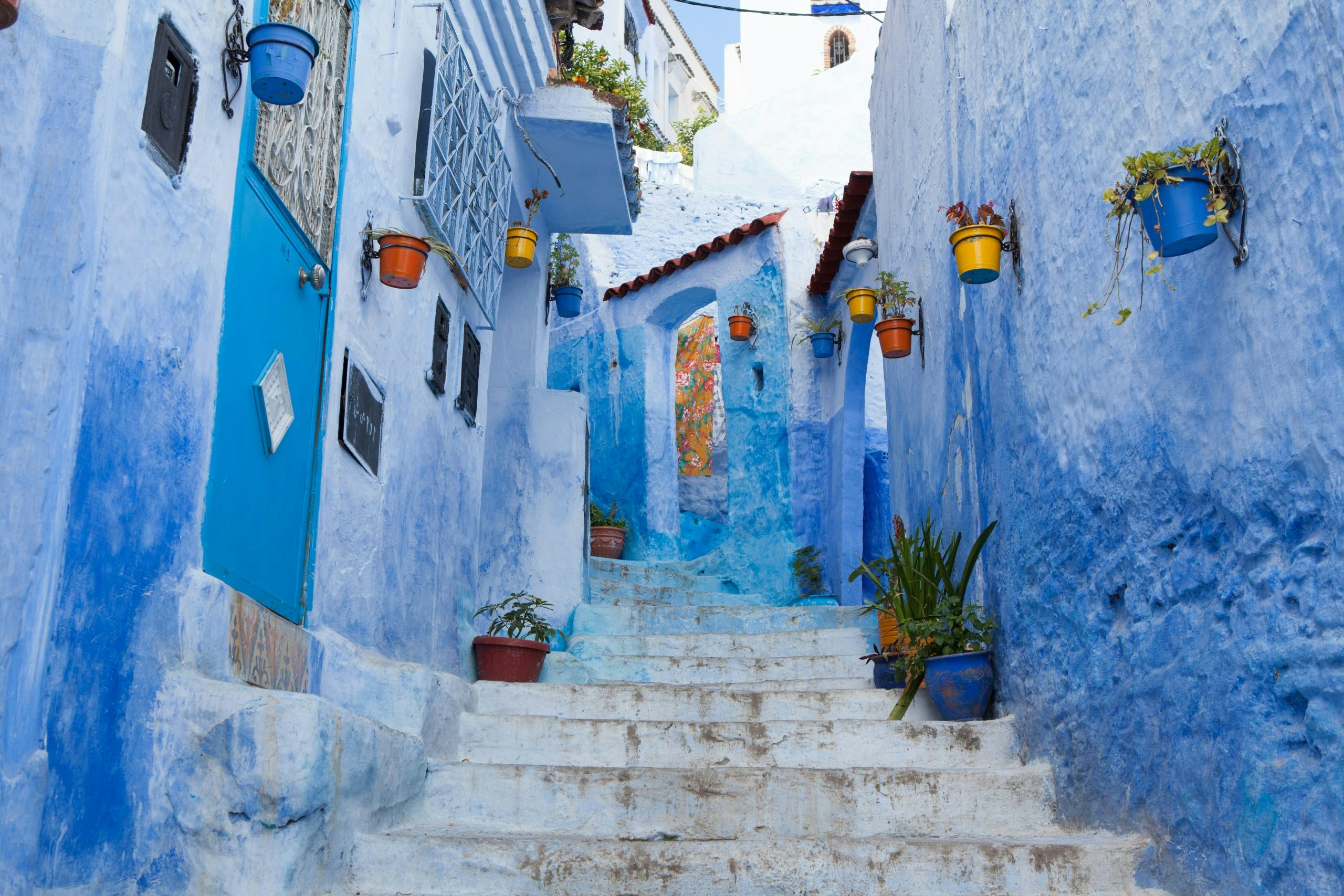 Narrow blue street in Chefchaouen lined with potted plants