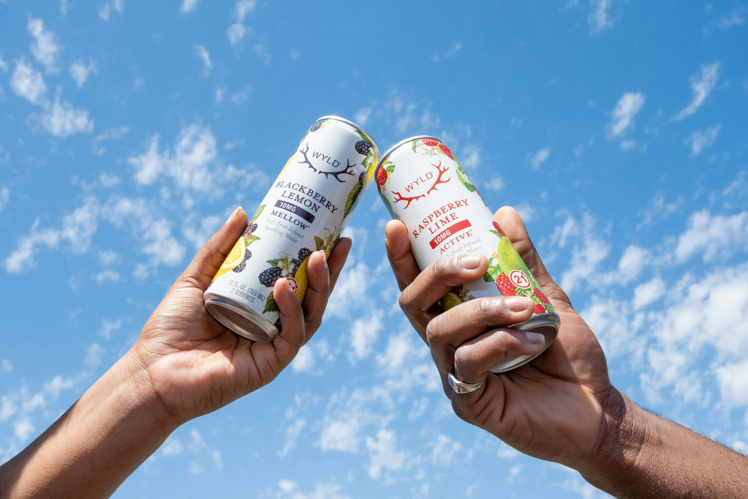 Two Wyld beverage cans clinking together against the sky