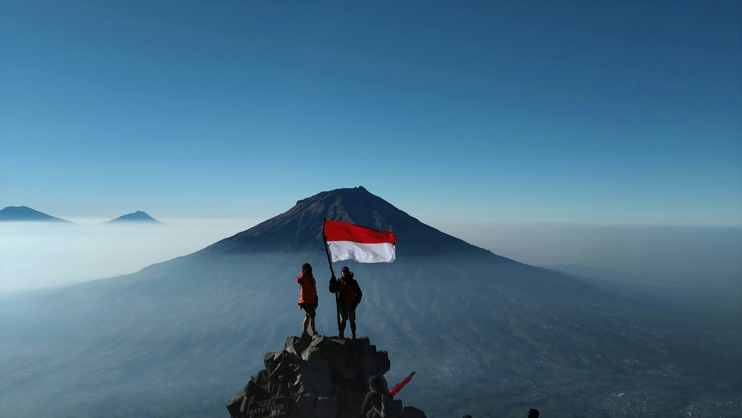 Hikers standing on a mountain summit in Indonesia holding the Indonesian flag