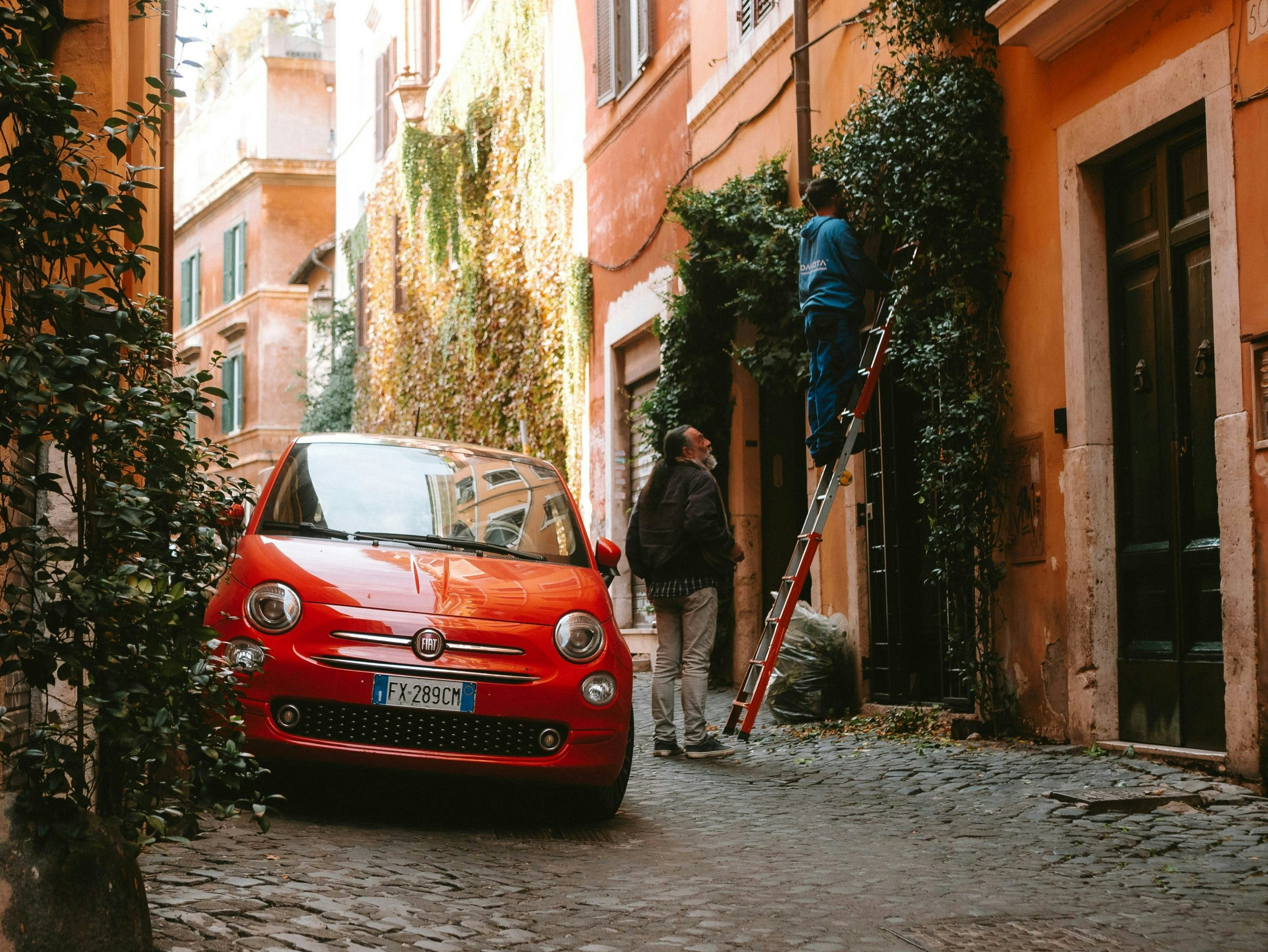 Person standing beside a classic Fiat on a colorful street in Rome, Italy