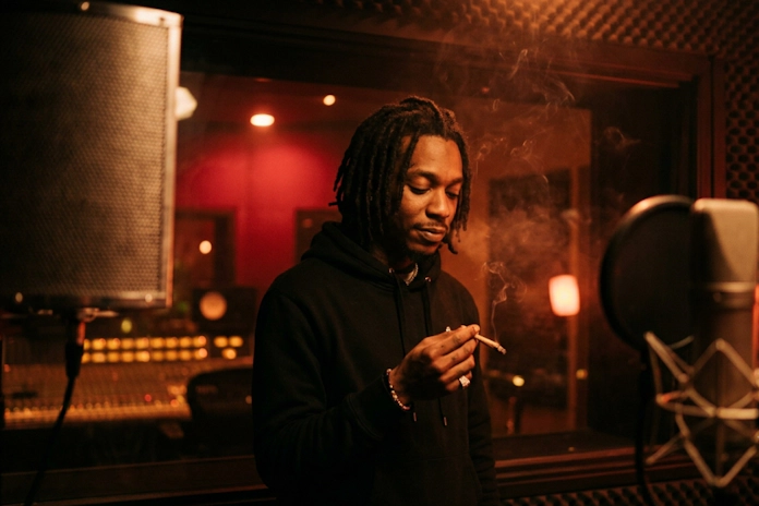Rapper holds lit joint in booth behind glass reflection