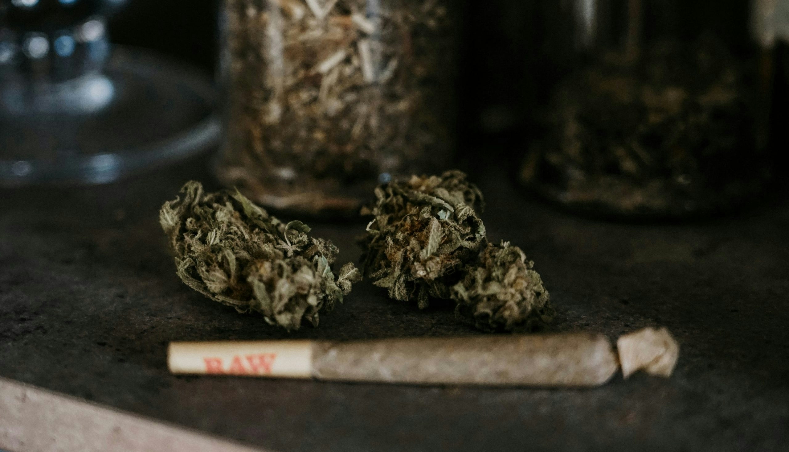 A rolled weed joint sitting in front of dense nugs.