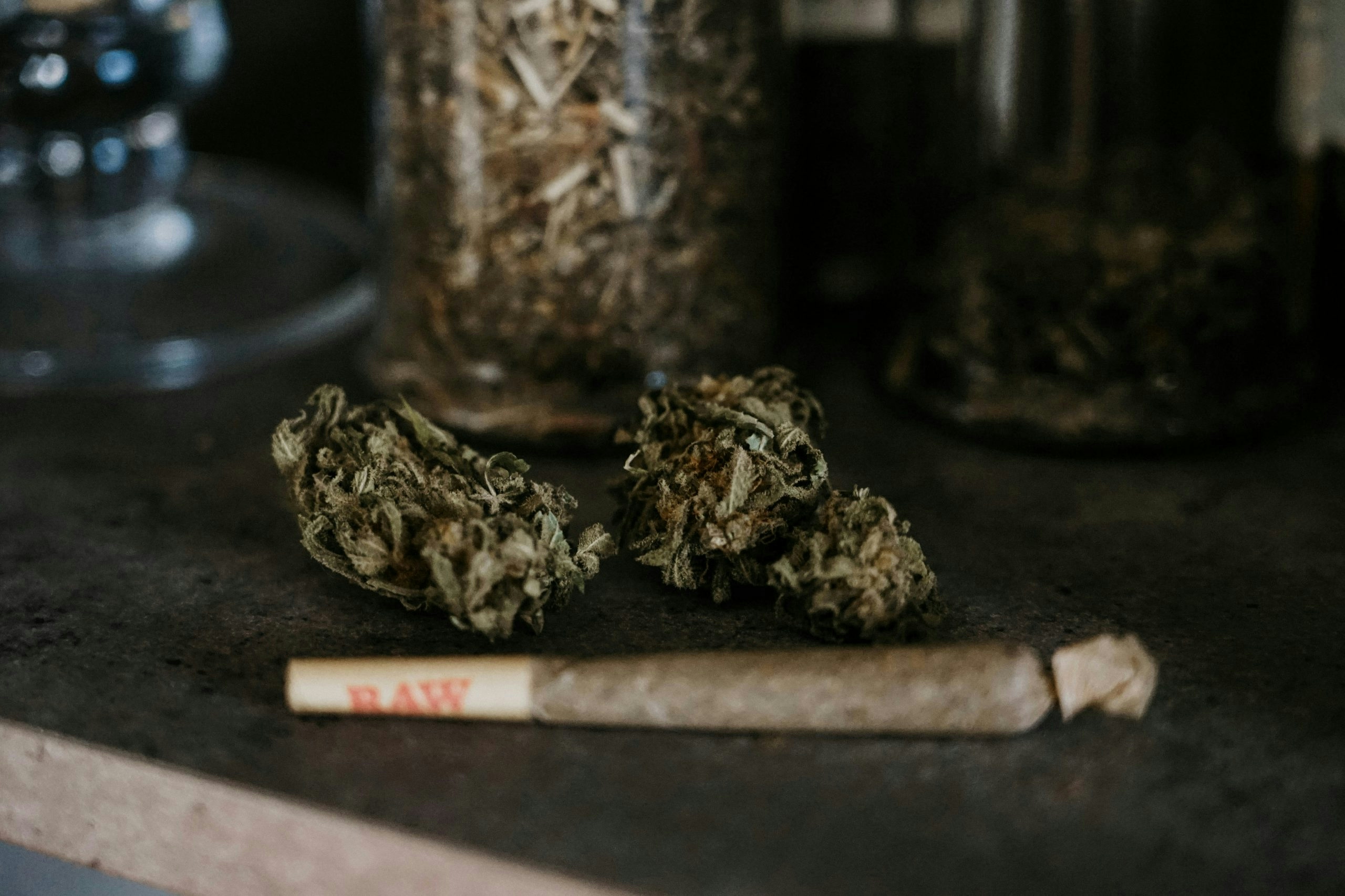 A rolled weed joint sitting in front of dense nugs.