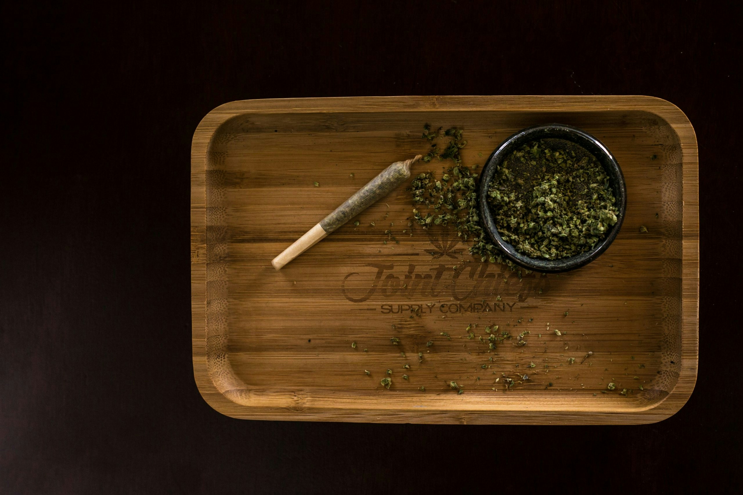 A rolled joint and a full grinder sitting on top of a wooden rolling tray.