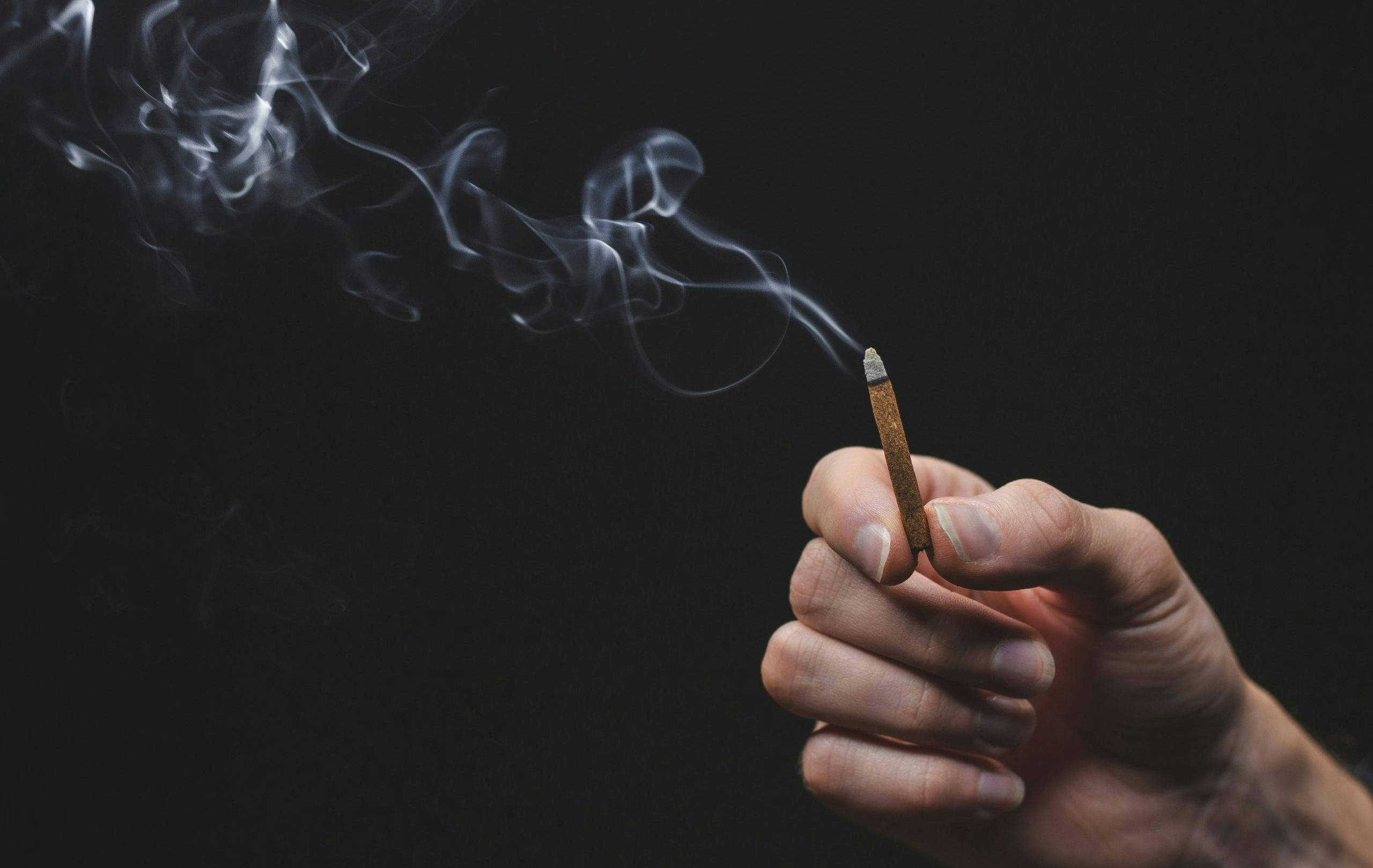 A single hand holding a lit, smoking joint.