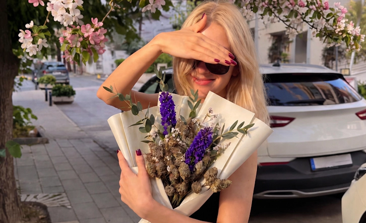 Woman posing with an elegant bouquet featuring purple flowers and cannabis buds